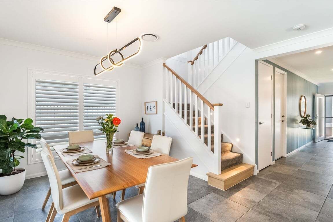 Un coin repas avec une table en bois, des chaises blanches et un escalier doté de rampes en bois.