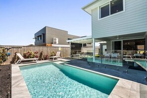 Ett modernt hus med en swimmingpool, en täckt uteplats och ett trästaket.