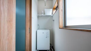 A compact bathroom with a white heater, a shelf with a cup, and a window. - TAISHO-7 (Osaka)