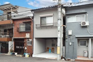 A residential building with a grey facade, a visible air conditioning unit, and a metal staircase leading to a balcony. - TAISHO-7 (Osaka)