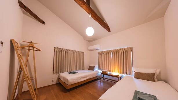 A room with two beds, a wooden ladder, a table with a lamp, and a hanging light fixture. - TAISHO-7 (Osaka)