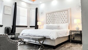 A modern bedroom with a tufted headboard, a grey bench, a bedside table with a lamp, and a chair. - Modern upscale home with an amazing kitchen. (El Paso)