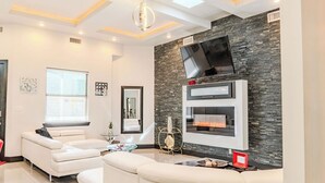 A modern living room with a stone accent wall, a flat-screen TV, and a fireplace. - Modern upscale home with an amazing kitchen. (El Paso)