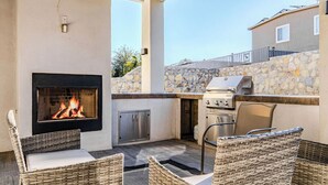 An outdoor patio with a stone wall, a grill, a fire pit, wicker chairs, and a view of a building in the background. - Modern upscale home with an amazing kitchen. (El Paso)