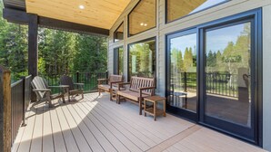 Una terraza de madera con mobiliario exterior y grandes ventanales.