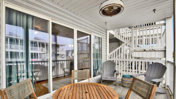 A covered outdoor seating area with a round wooden table and four chairs, a staircase, and a view of a residential building. - Beachside Retreat, Steps from the Beach | Heated Pool Access (Tybee Island)