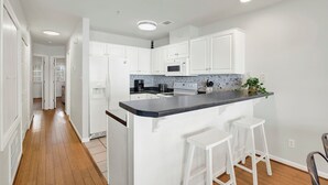 A modern kitchen with white cabinets, a black countertop, and two white bar stools. - Beachside Retreat, Steps from the Beach | Heated Pool Access (Tybee Island)