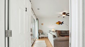 A hallway leading to a living room with a sofa, a lamp, and wall decorations. - Beachside Retreat, Steps from the Beach | Heated Pool Access (Tybee Island)