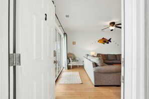 A hallway leading to a living room with a sofa, a lamp, and wall decorations. - Beachside Retreat, Steps from the Beach | Heated Pool Access (Tybee Island)