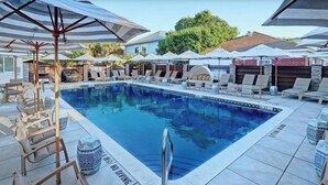 A swimming pool with lounge chairs and umbrellas, surrounded by a tiled deck. - Beachside Retreat, Steps from the Beach | Heated Pool Access (Tybee Island)