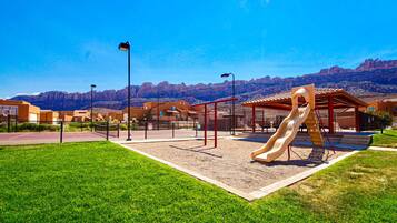 Ein Spielplatz mit einer Rutsche, umgeben von einem Zaun, mit einer Bergkette im Hintergrund.