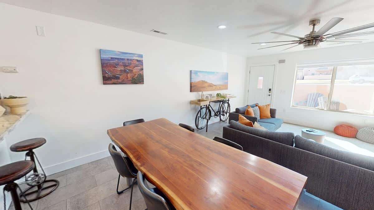 A modern living room with a wooden dining table, bar stools, a sofa, and a bicycle.