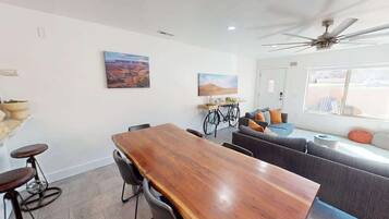 A modern living room with a wooden dining table, bar stools, a sofa, and a bicycle.