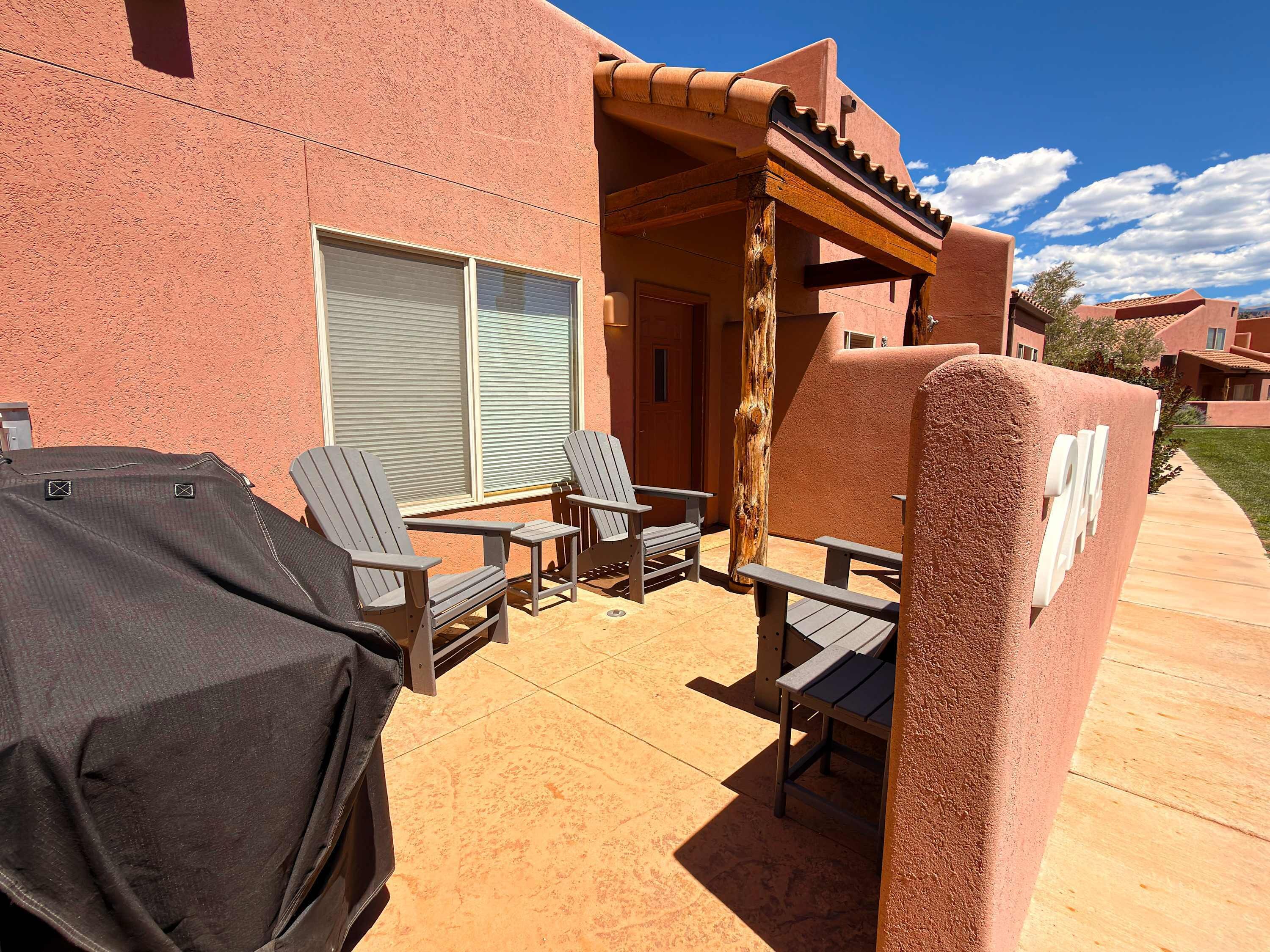 An outdoor patio with two Adirondack chairs, a barbecue grill, and a covered table.