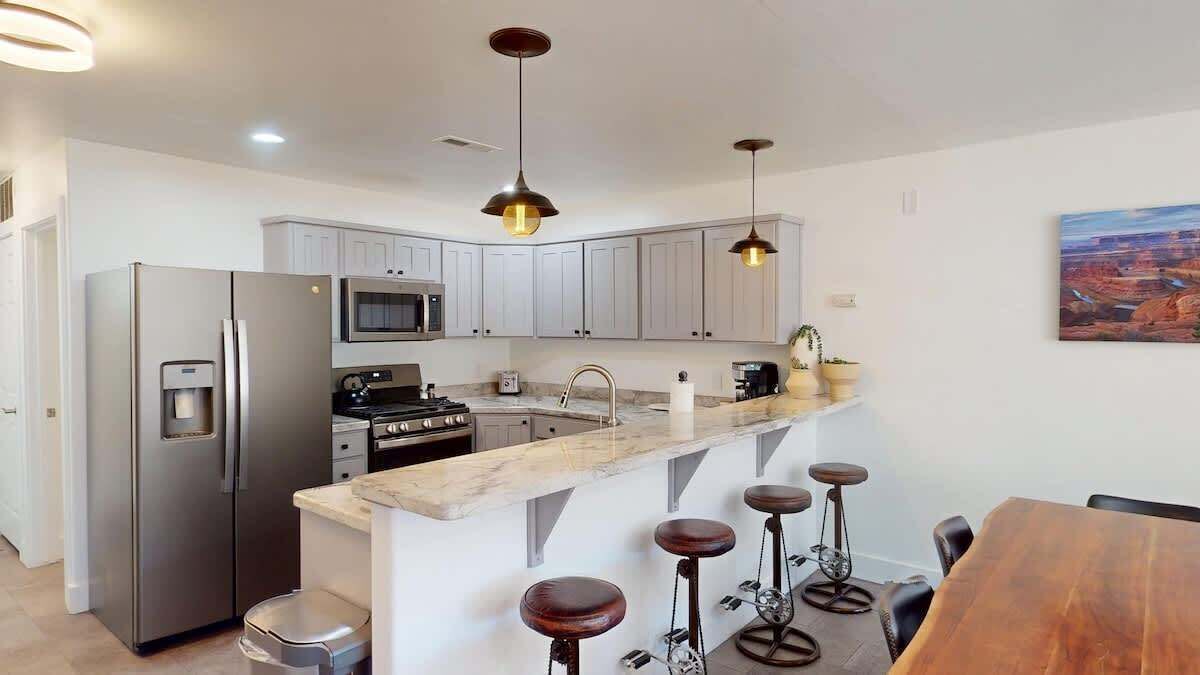 A modern kitchen with stainless steel appliances, a marble countertop, and bar stools.