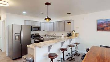 A modern kitchen with stainless steel appliances, a marble countertop, and bar stools.