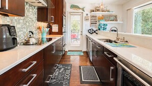 A modern kitchen with wooden cabinets, a coffee maker, and a kettle. - Aqua Vie - 4 BR Retreat w/Private Pool, Hot Tub, Elevator (Southern Shores)