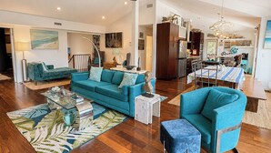 A spacious living area with a teal sofa, a coffee table, and a dining table with chairs. - Aqua Vie - 4 BR Retreat w/Private Pool, Hot Tub, Elevator (Southern Shores)