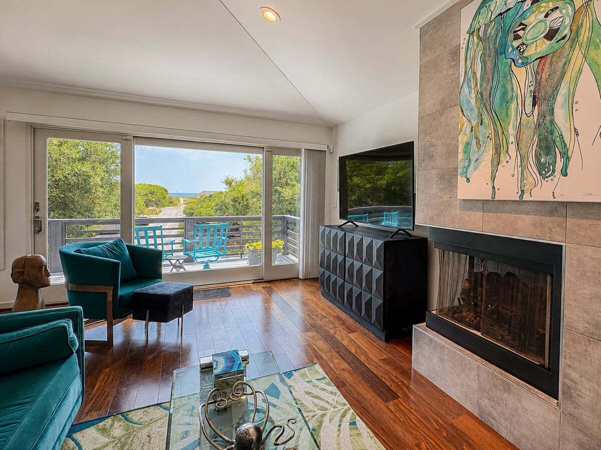 A modern living room with a fireplace, teal furniture, and a large window overlooking a balcony.