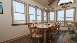 Un comedor con mesa y sillas de madera, ventanas amplias con vistas y un ventilador de techo.