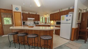 A kitchen with wooden cabinets, a central island with stools, a refrigerator, and a microwave. - HappyTauk - 4 BR Home Near Beach w/Private Pool - Dogs Allowed (Southern Shores)