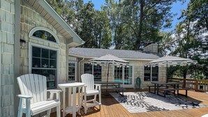 Um deck de madeira com cadeiras Adirondack, uma piscina e guarda-sóis.