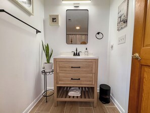 A bathroom with a wooden vanity, a mirror, a sink, a plant, and a trash bin. - One Particular Harbour - 5 BR Single Level Ranch, Private Pool, Canalfront (Southern Shores)
