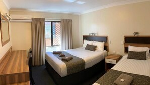 Ein Hotelzimmer mit einem großen Bett, einem kleineren Bett, einem Schreibtisch und einem Stuhl. Es gibt ein Fenster mit Vorhängen, einen Nachttisch und eine Lampe.