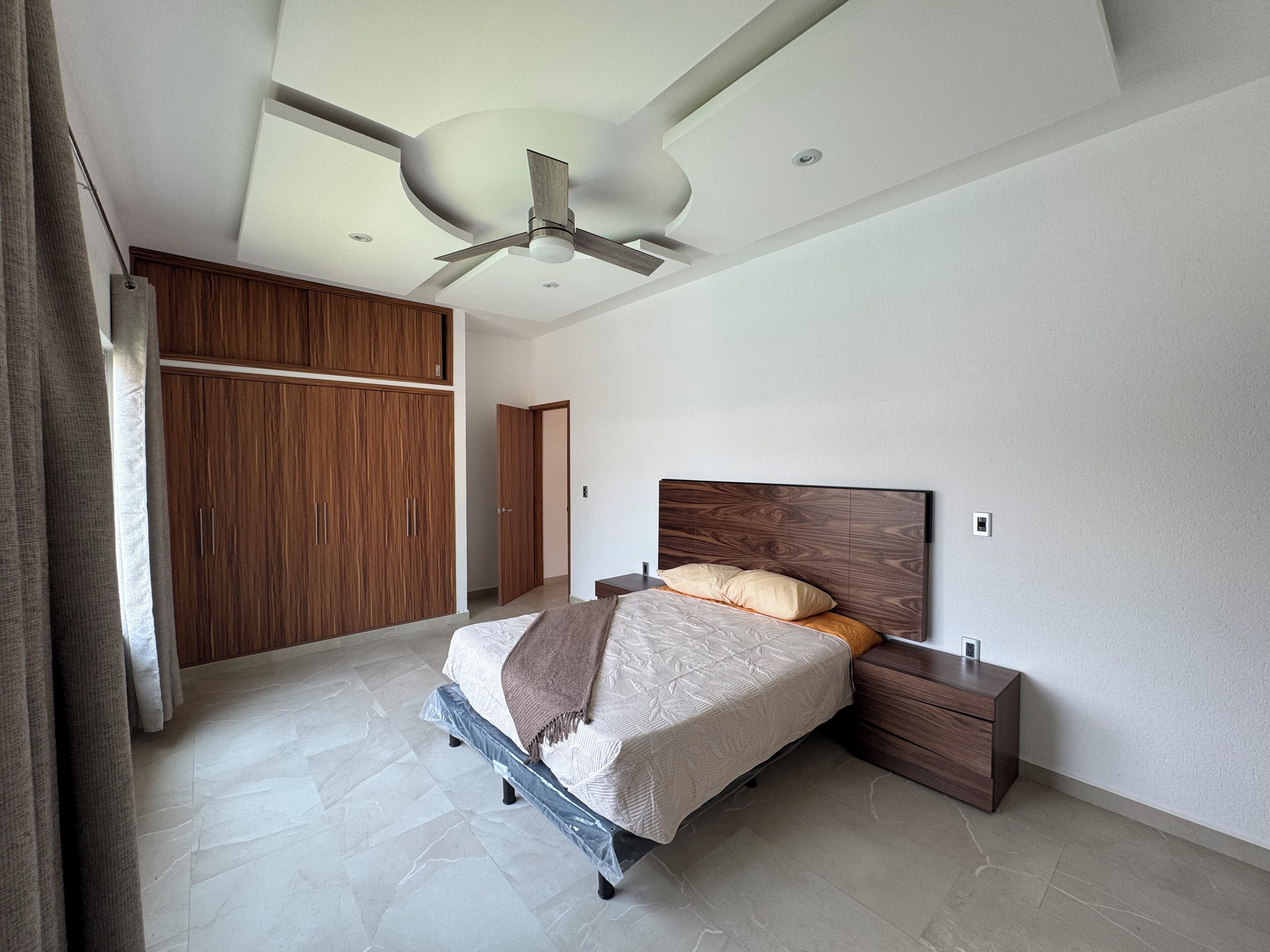 Een moderne slaapkamer met een bed, een houten garderobe, een plafondventilator en een nachtkastje.
