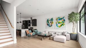 Ein modernes Wohnzimmer mit Treppe, einer Küche und zwei abstrakten Gemälden.