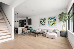 A modern living room with a staircase, a kitchen, and two abstract paintings. - Modern Palette - Private Patio - Mins to Broadway (Nashville)