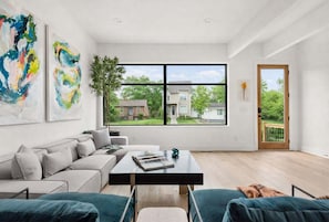 A modern living room with a large window, a sofa, a coffee table, and abstract art on the wall. - Modern Palette - Private Patio - Mins to Broadway (Nashville)