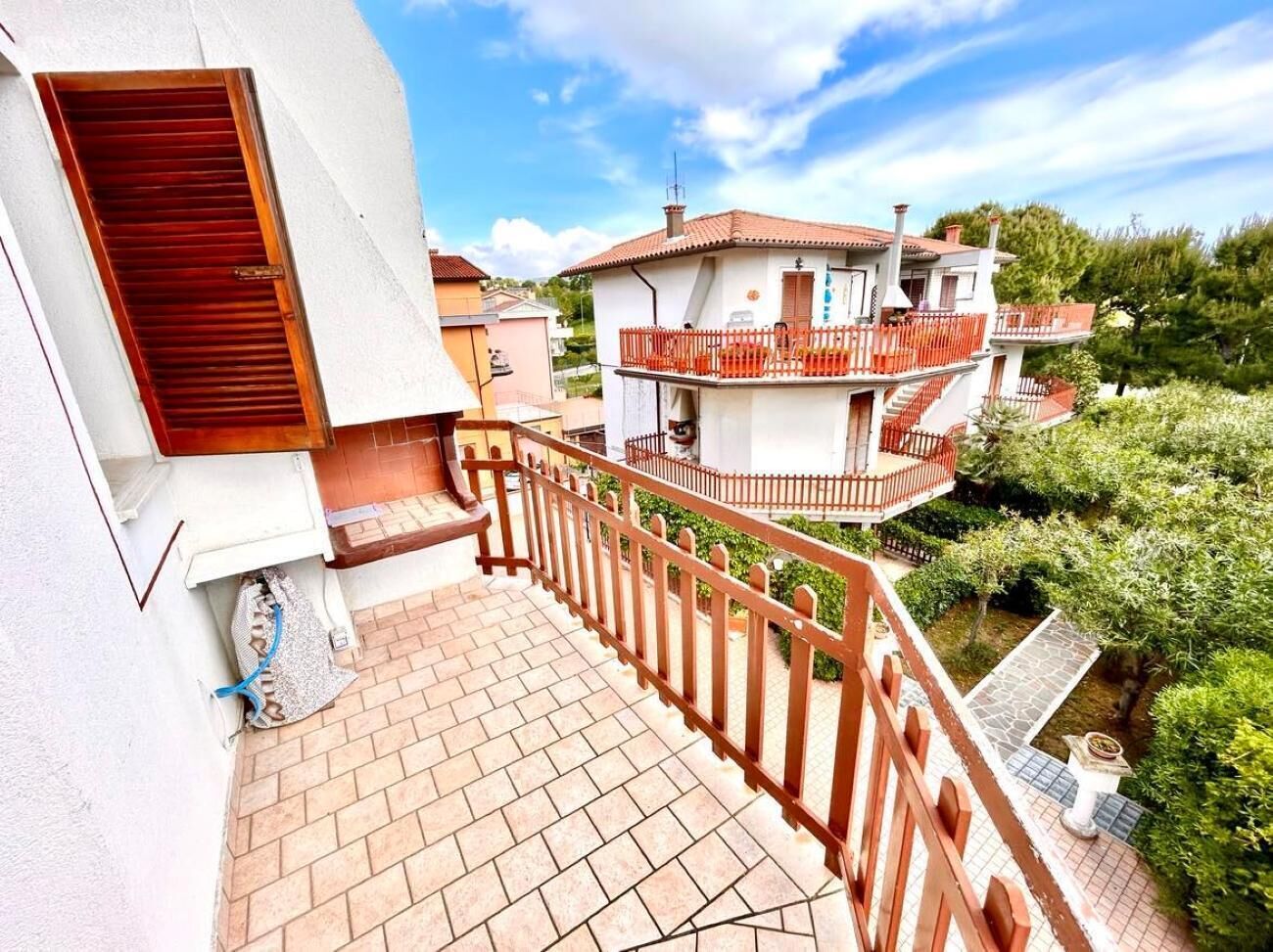 A residential building with a tiled balcony, a red railing, and a garden area.