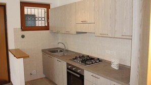 Eine kleine Küche mit hellen Holzschränken, einem Gasherd, einer Spüle und einem Fenster mit Gitterstäben.