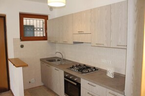 A small kitchen with light wood cabinets, a gas stove, a sink, and a window with bars. - Cristina apartment in Sirolo with garden (Sirolo)