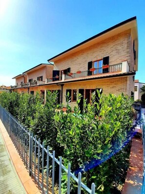 A two-story building with a brick facade, multiple balconies, and a garden area with neatly trimmed bushes. - Cristina apartment in Sirolo with garden (Sirolo)