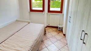 Ein Schlafzimmer mit Bett, zwei Fenstern, einem Heizkörper und einem Kleiderschrank.