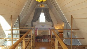 Une chambre mansardée chaleureuse avec un plafond en bois, un lit recouvert d’une literie à motifs et un luminaire suspendu.