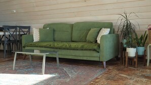 Un canapé vert agrémenté de coussins à motifs, une petite table et un tapis à motifs dans une pièce aux murs en bois et ornée de plantes en pot.