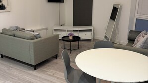 A modern living room with a grey sofa, a white round table, and grey chairs. A flat-screen TV is mounted on the wall, and a large mirror is leaning against the wall. - Stylish Central Southampton 2-Bed Apartment Perfect for all types of Travelers & (Southampton)