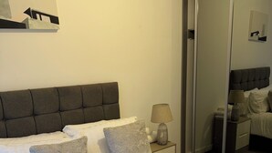 A neatly made bed with a tufted headboard, a bedside lamp, and a mirror on the wall. - Stylish Central Southampton 2-Bed Apartment Perfect for all types of Travelers & (Southampton)