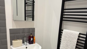 A modern bathroom with a white sink, a mirror, a towel rack with a white towel, and a small black storage unit. - Stylish Central Southampton 2-Bed Apartment Perfect for all types of Travelers & (Southampton)