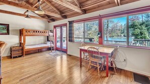 A cabin with a wooden bunk bed, a dining table with chairs, large windows, and a view of a lake. - Lakefront Lodge w/Dock, Wood Fireplace, Kayaks & Modern Kitchen (Nevada City)