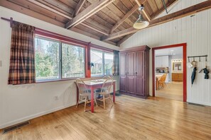 A dining area with a wooden table and chairs, a window with plaid curtains, and a view of the outdoors. - Lakefront Lodge w/Dock, Wood Fireplace, Kayaks & Modern Kitchen (Nevada City)