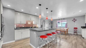 A modern kitchen with white cabinets, a central island with red stools, and pendant lighting. - Lakefront Lodge w/Dock, Wood Fireplace, Kayaks & Modern Kitchen (Nevada City)