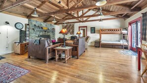 A rustic interior with exposed wooden beams, a stone fireplace, a bunk bed, and a cozy seating area. - Lakefront Lodge w/Dock, Wood Fireplace, Kayaks & Modern Kitchen (Nevada City)