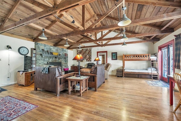 A rustic interior with exposed wooden beams, a stone fireplace, a bunk bed, and a cozy seating area.