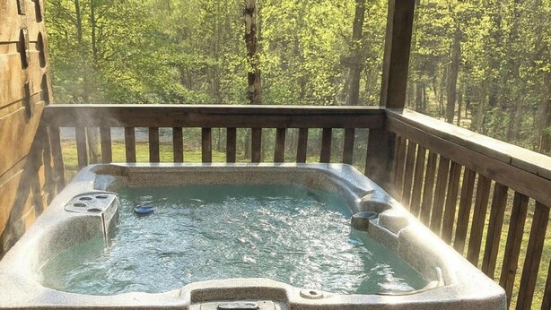 Een hottub met een houten terras en uitzicht op een bos.