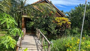 A wooden pathway leading to a building with a tiled roof, surrounded by lush greenery and flowering plants. - PHU QUOC POMELO GARDEN (Phu Quoc)