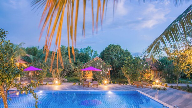 A swimming pool with lounge chairs and umbrellas, surrounded by tropical vegetation and small structures. - PHU QUOC POMELO GARDEN (Phu Quoc)